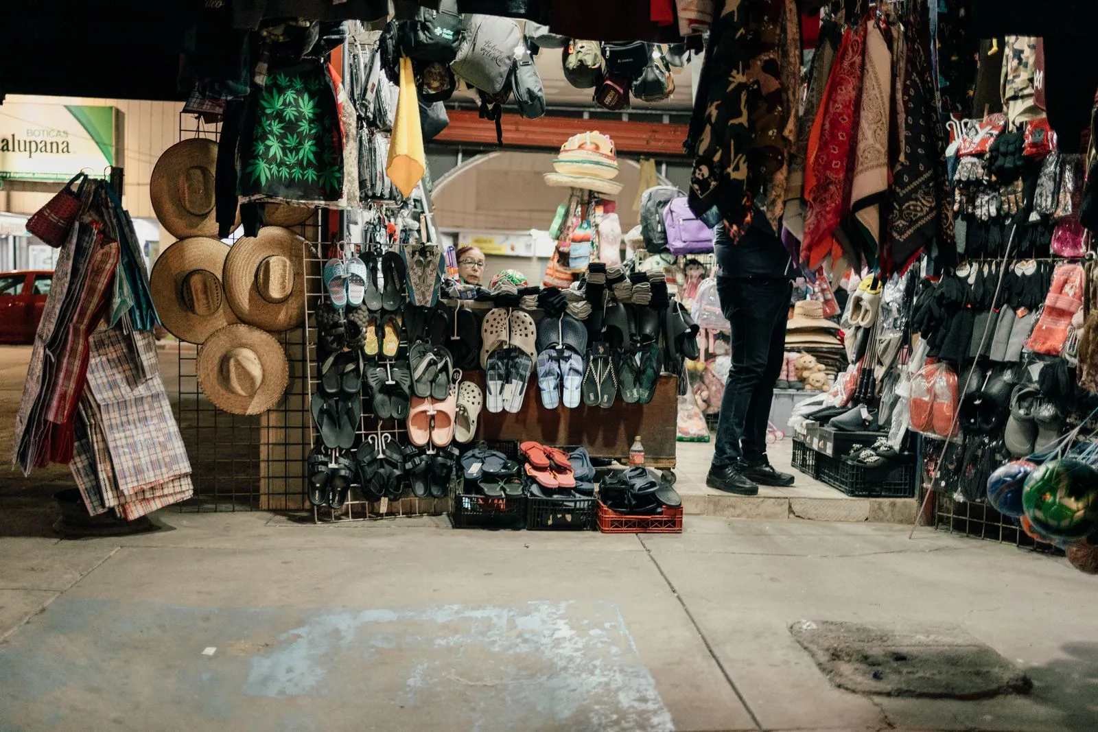 Diverse market stall at night showcasing hats, shoes, and colorful textiles.
